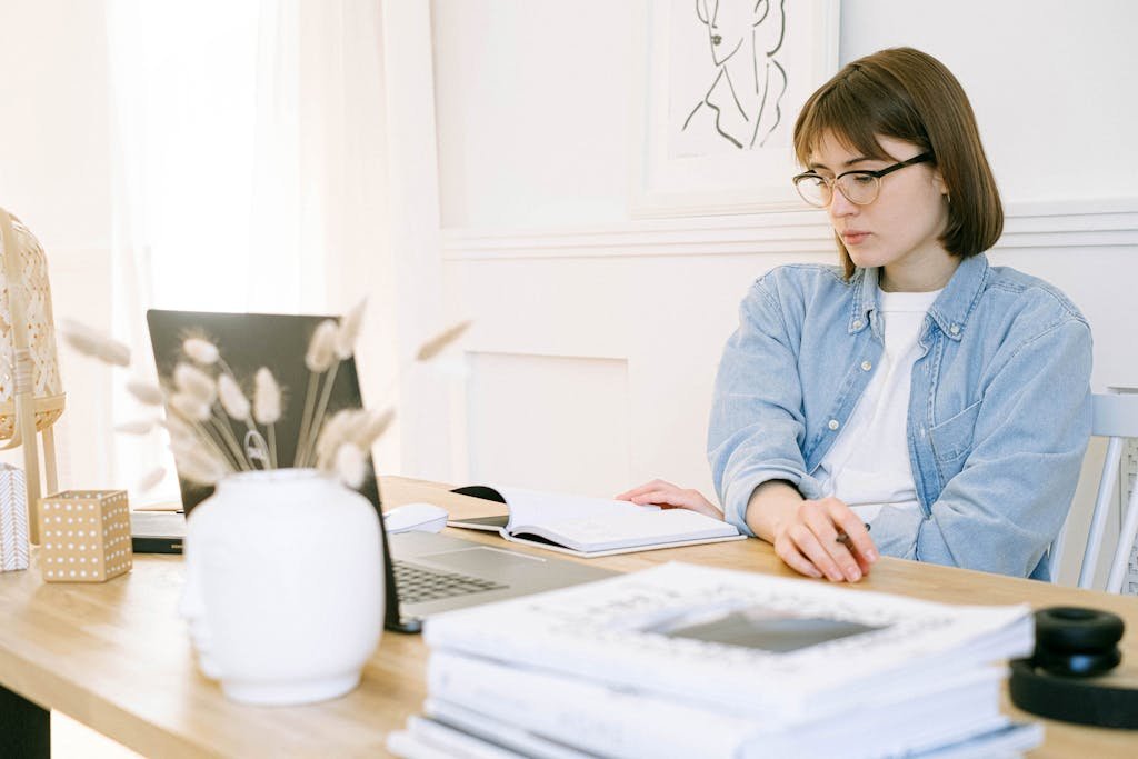 Woman working in a stylish home office, taking notes with laptop open on desk.