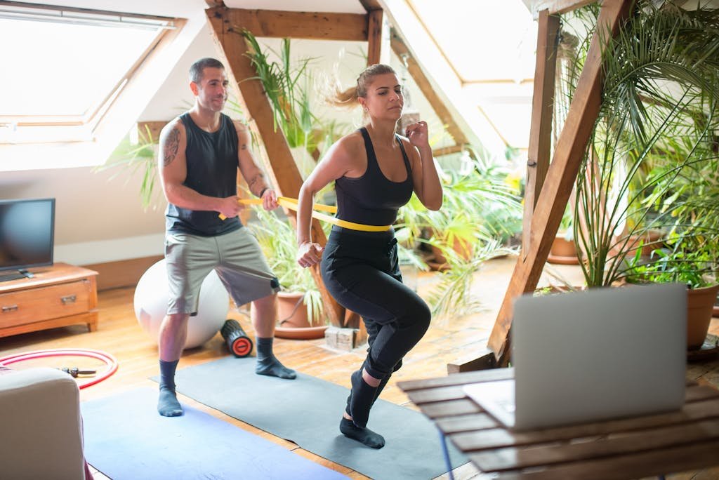 A couple working out on yoga mats indoors, using a laptop for guidance.