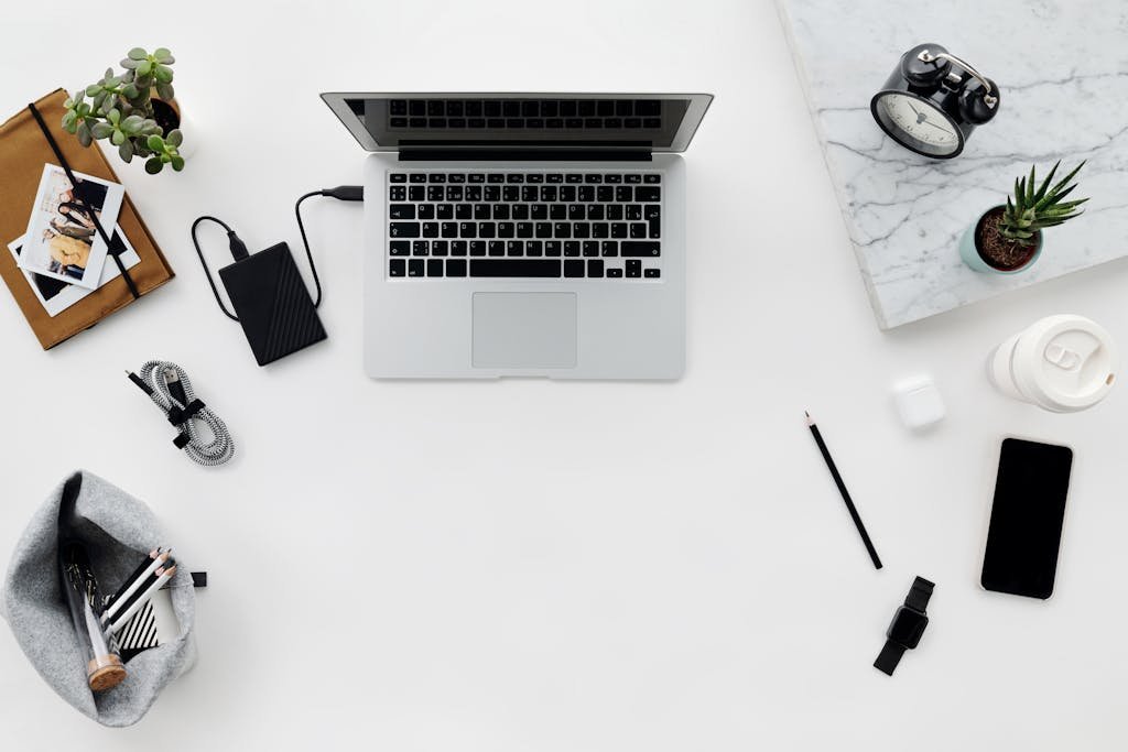 Organized flat lay of a clean workspace with laptop, gadgets, and plants on a white table.