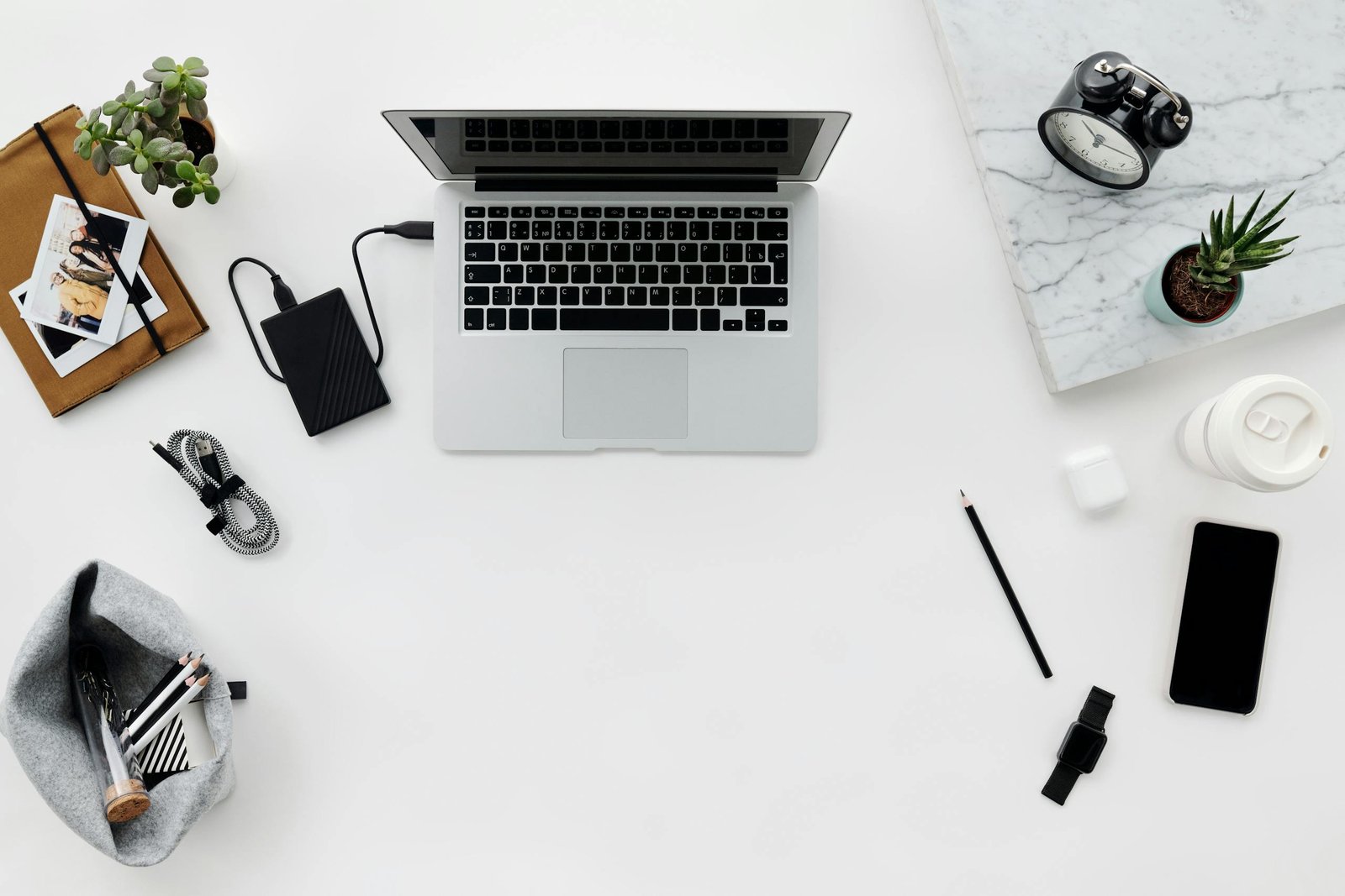 Organized flat lay of a clean workspace with laptop, gadgets, and plants on a white table.
