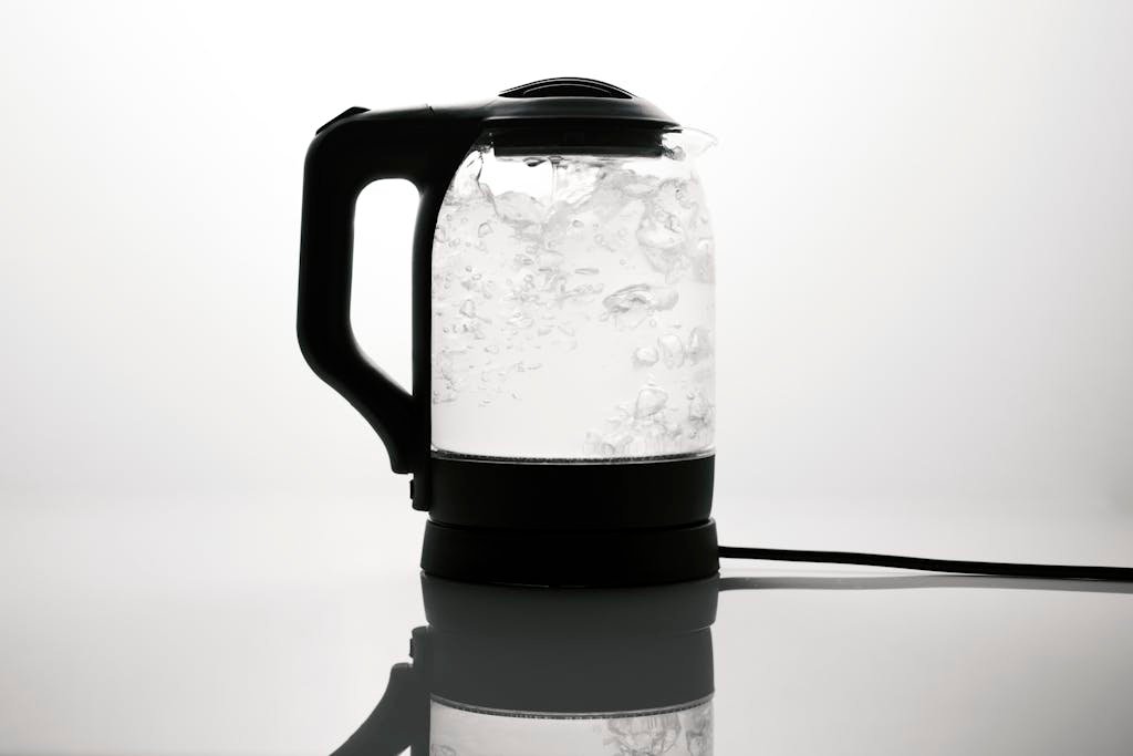 A sleek electric kettle boiling water, captured on a reflective white surface.