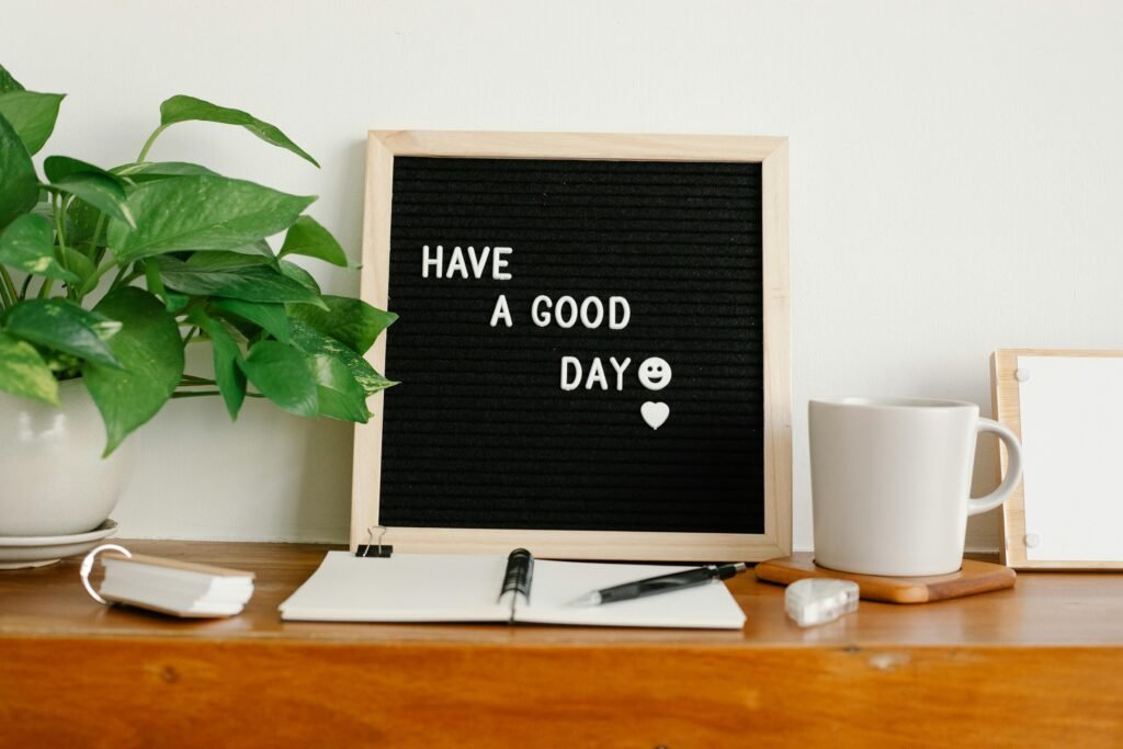 Various stationery and mug of hot beverage placed on shelf near board with Have A Good Day inscription and potted plant